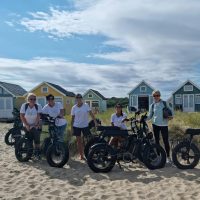 group of friends on electric bikes on a beach with beach huts